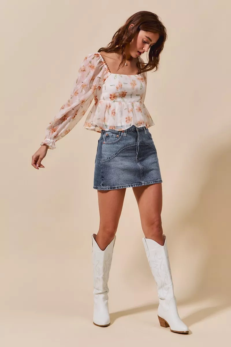 Woman wearing a floral blouse, denim skirt, and white knee-high boots on a beige background