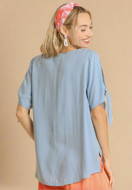 Woman wearing a dusty blue top with tied sleeves on a beige background