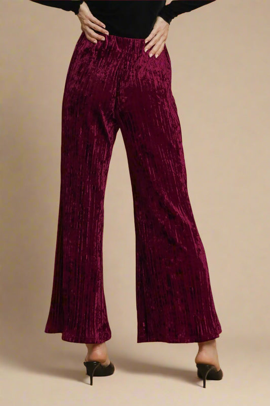 Burgundy velvet wide-leg pants worn by a person on a beige background