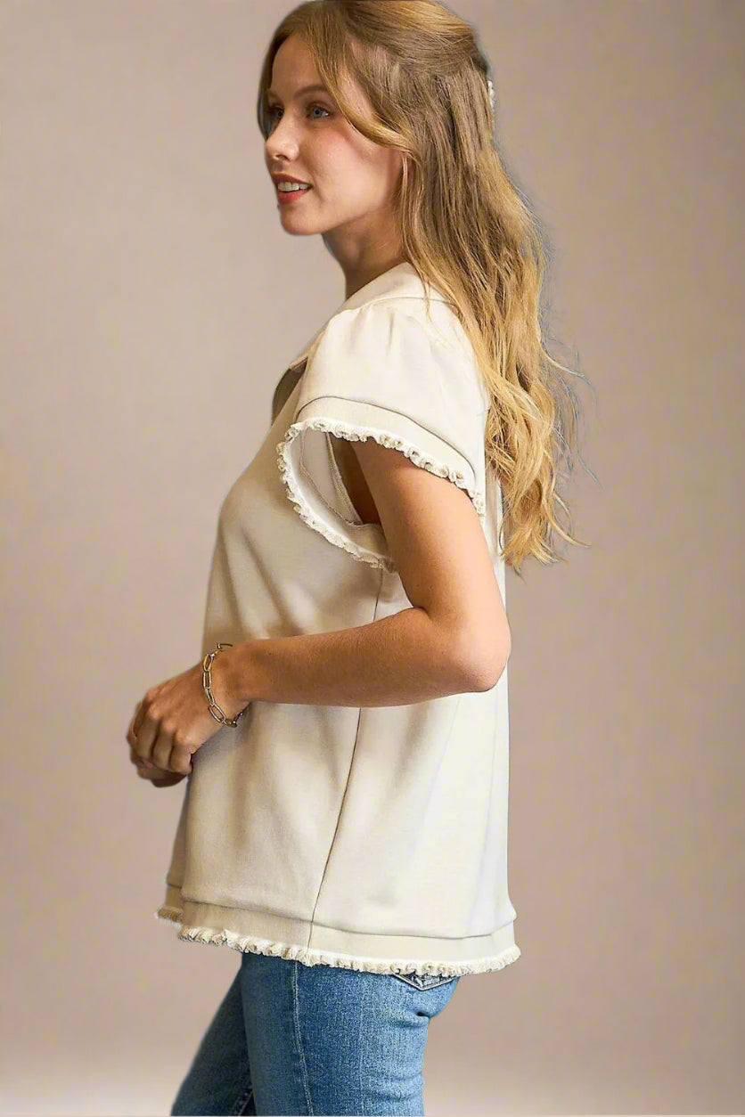 Woman wearing a beige blouse with ruffled sleeves against a beige background