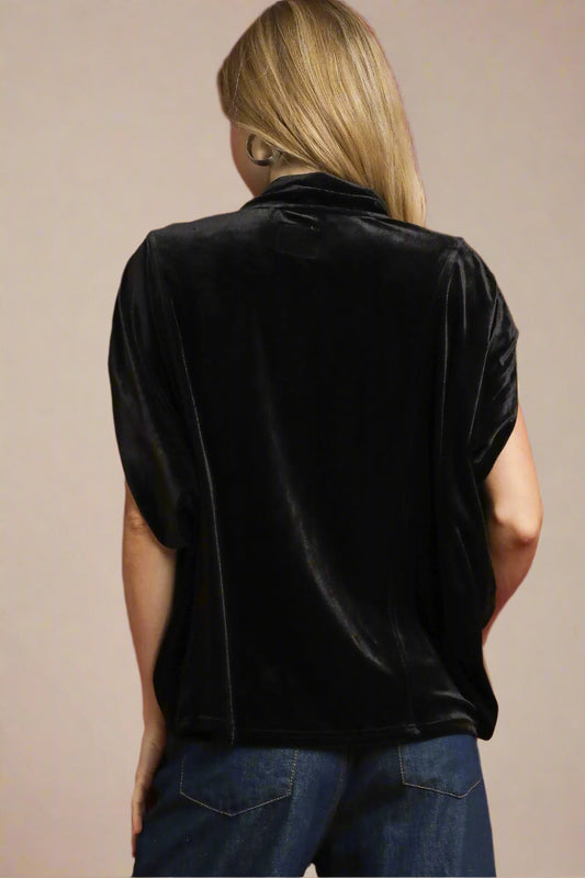 Person wearing a black velvet top against a beige background