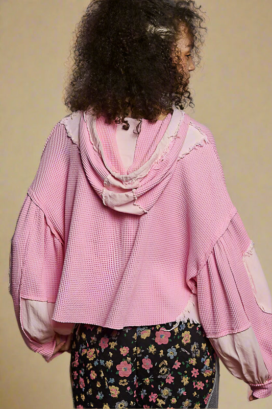 Person wearing a pink textured top with floral skirt against a beige background
