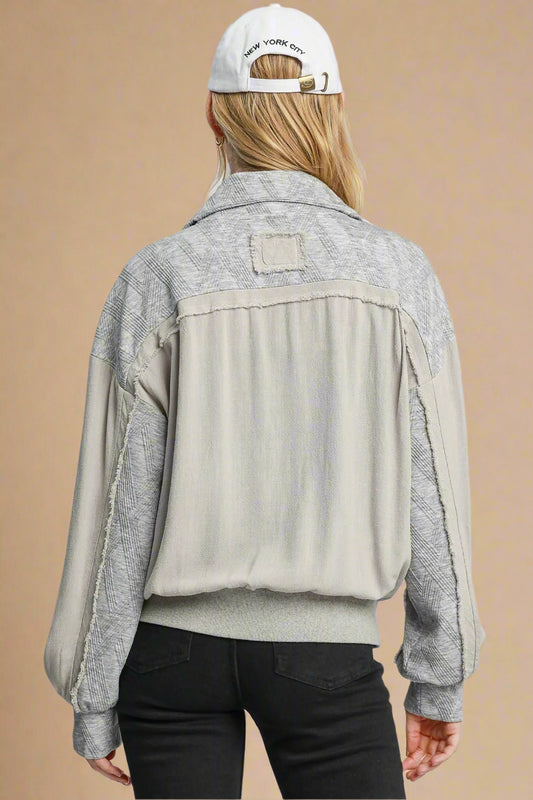 Person wearing a gray and beige jacket with a white cap on a plain background