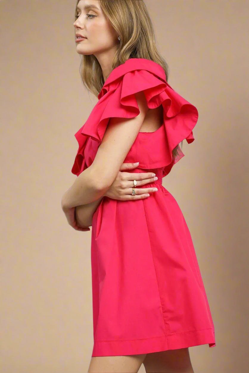 Woman wearing a bright pink dress with ruffled shoulders against a gray background