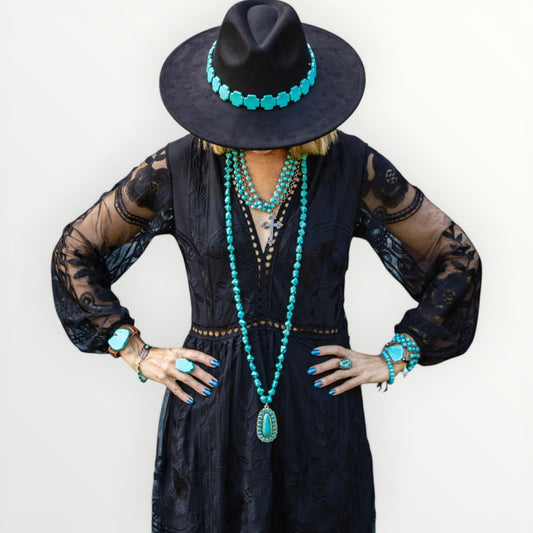Person wearing a black dress, hat, and turquoise jewelry against a white background