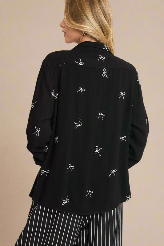 Black blouse with bow pattern worn by a person on a light background