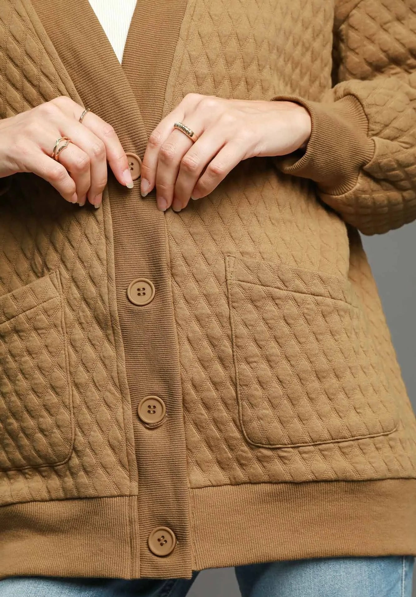 Close-up of a person wearing a brown quilted jacket with buttons, on a gray background.