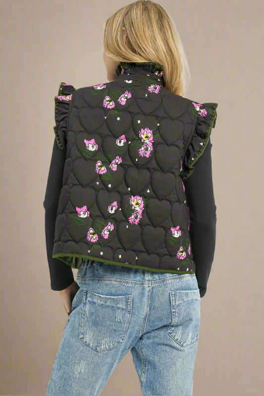 Person wearing a black quilted vest with pink floral patterns on a beige background