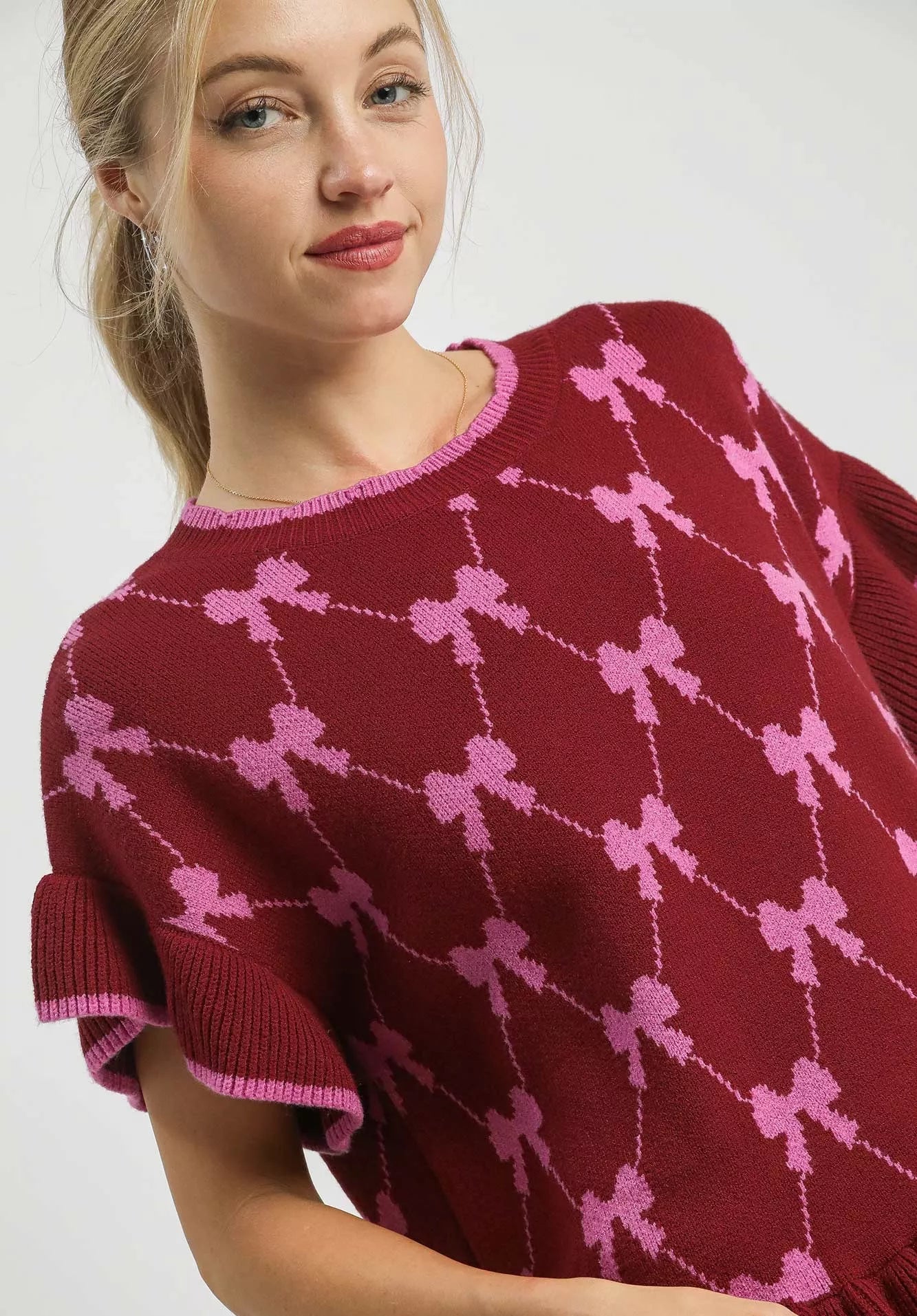 Woman wearing a burgundy sweater with pink bow pattern on a white background