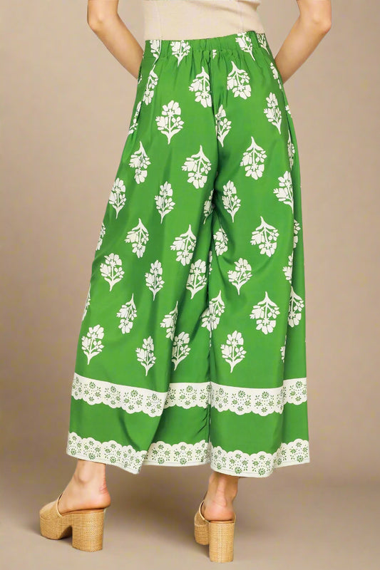Green pants with white floral pattern worn by a person on a white background
