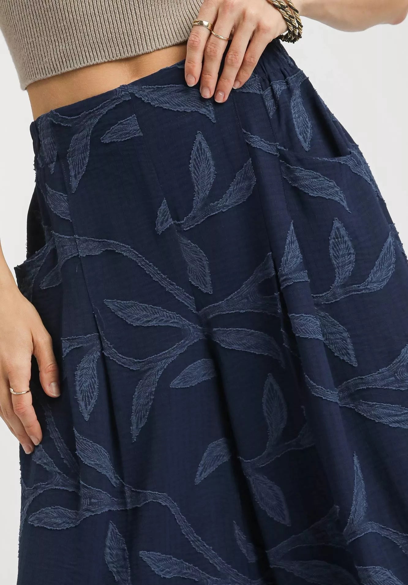 Navy blue skirt with leaf pattern worn by a person, on a white background.