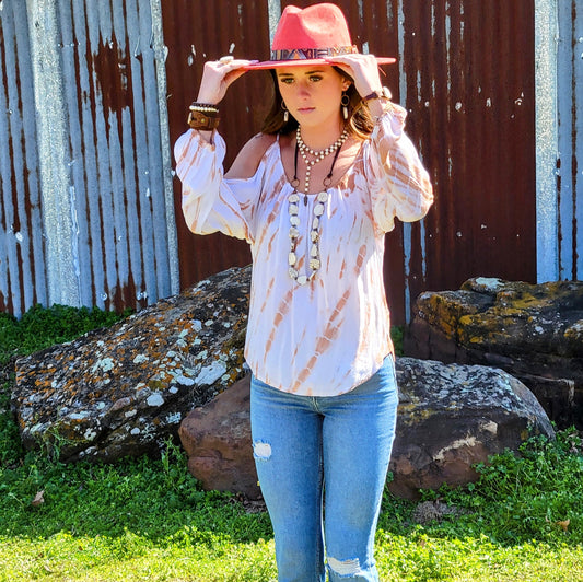 Woman wearing a tie-dye blouse and pink hat in front of a rustic metal wall.