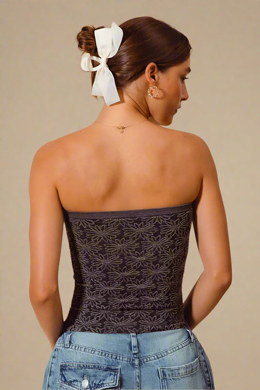 Woman wearing a strapless top with butterfly pattern and blue jeans against a beige background