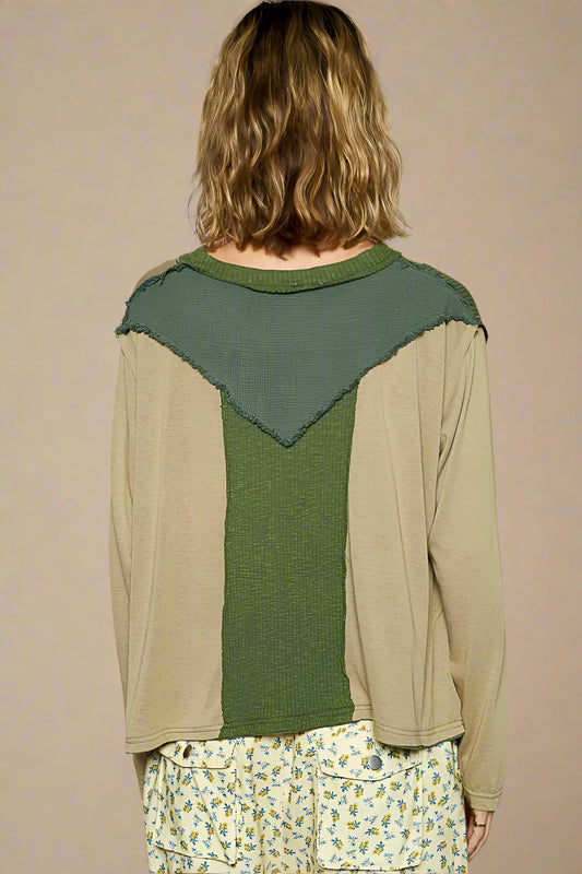 Person wearing a green and beige long-sleeve top with a geometric pattern on a plain background