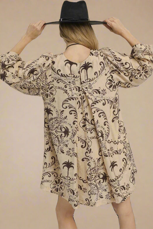 Person wearing a beige dress with black floral patterns and a black hat on a beige background