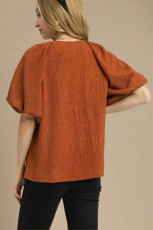 Person wearing a rust-colored textured top on a white background
