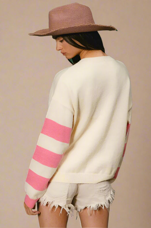 Person wearing a cream sweater with pink stripes and a brown hat against a green background
