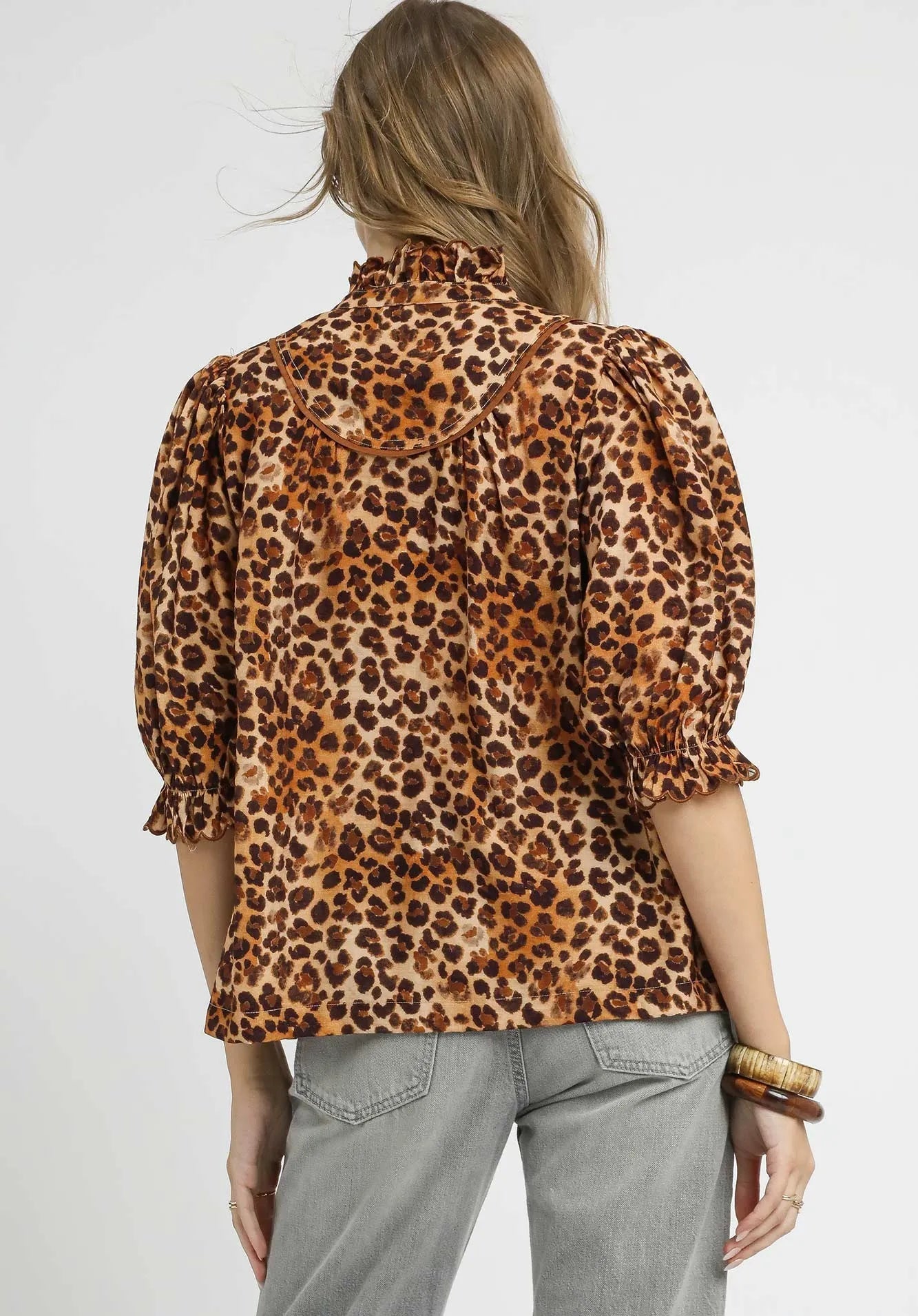 Person wearing a leopard print blouse with gray pants on a white background