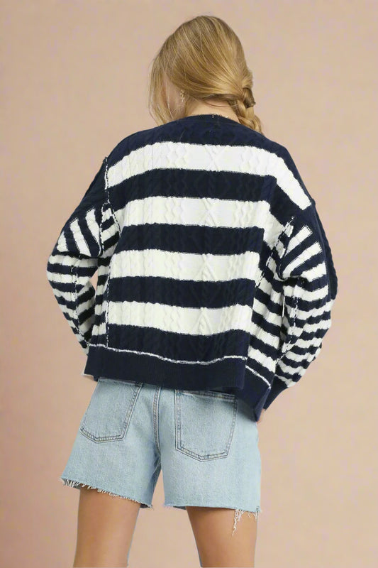 Person wearing a navy and white striped sweater with denim shorts on a plain background