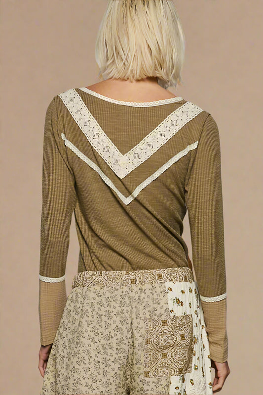 Person wearing a green long-sleeve top with lace details and patterned pants on a plain background