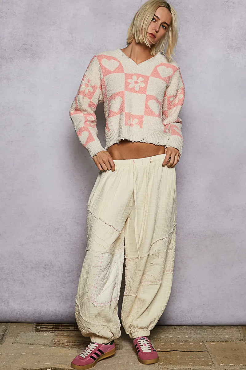 Woman wearing a patterned sweater and beige pants against a gray background