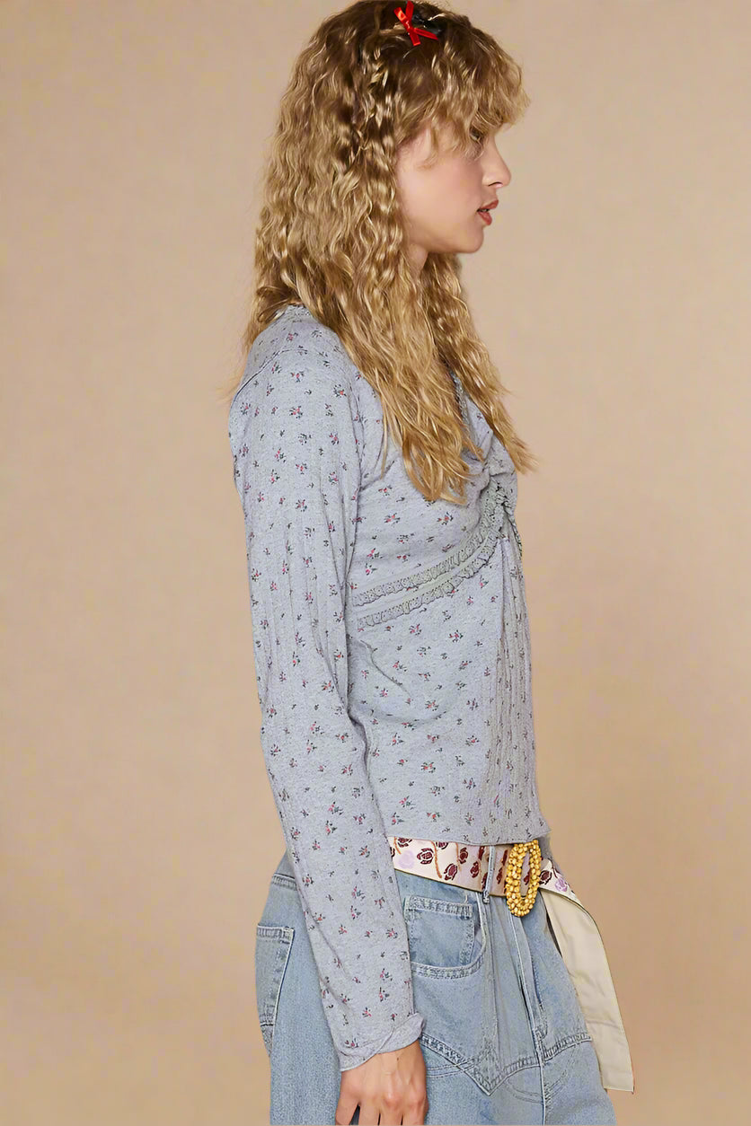 Woman wearing a light blue floral blouse and jeans against a beige wall