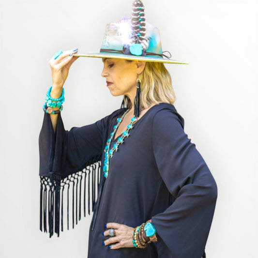 Woman wearing a dark blue dress with fringe, turquoise jewelry, and a decorative hat against a white background