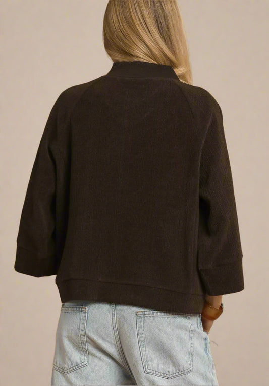 Person wearing a brown jacket and light blue jeans against a beige background