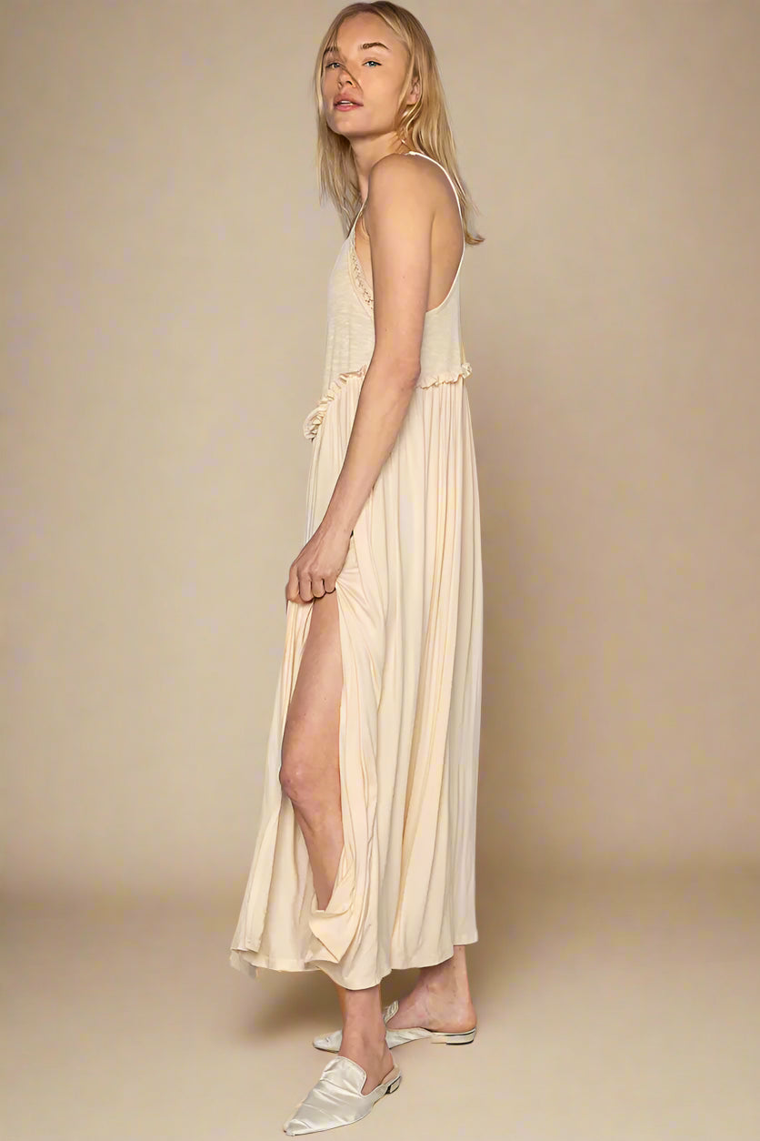 Woman wearing a long beige dress with a slit on a plain background
