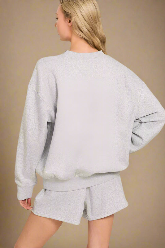 Person wearing a gray sweatshirt and shorts set on a beige background