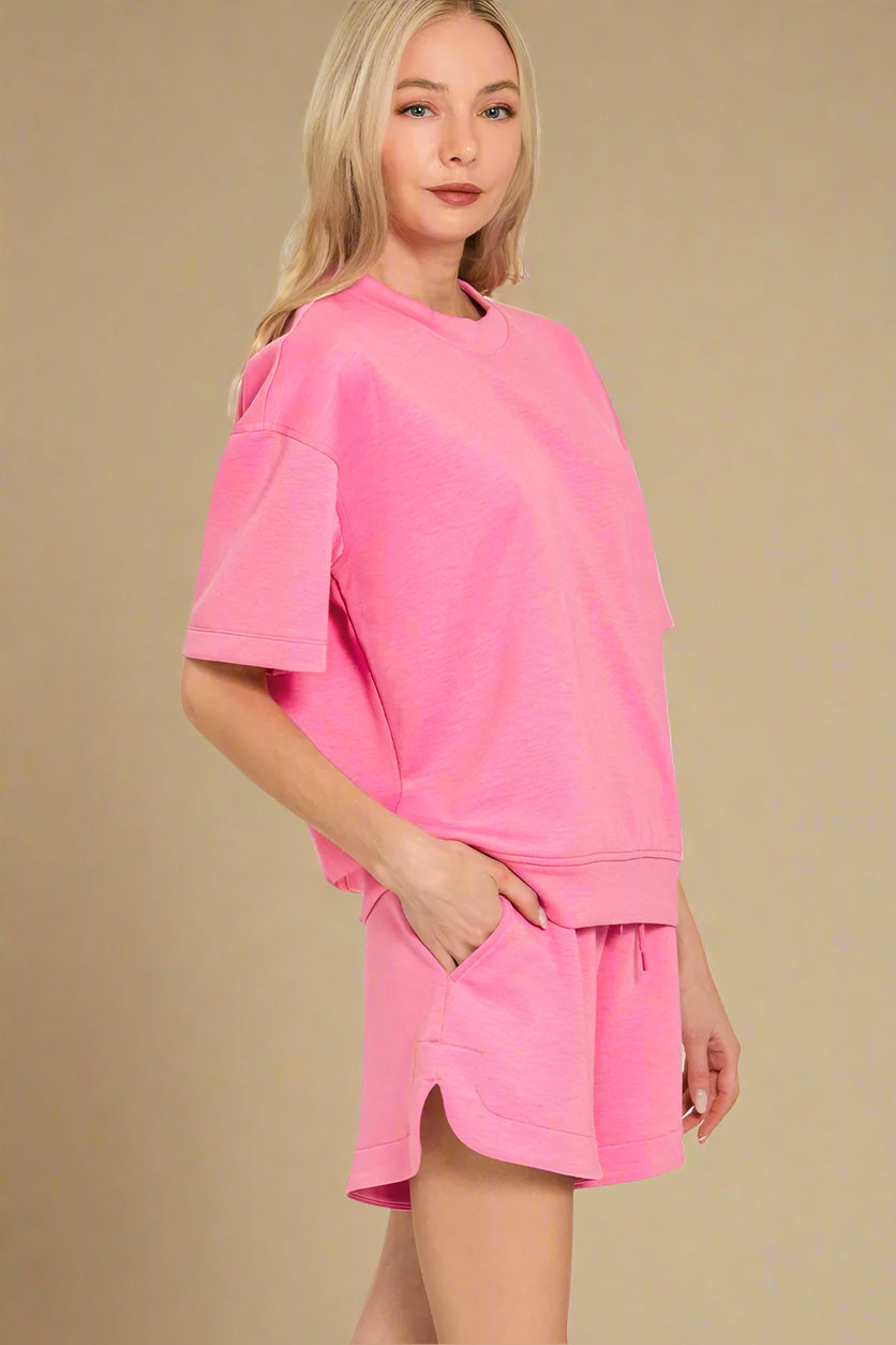 Woman wearing a pink oversized sweatshirt and shorts set on a beige background