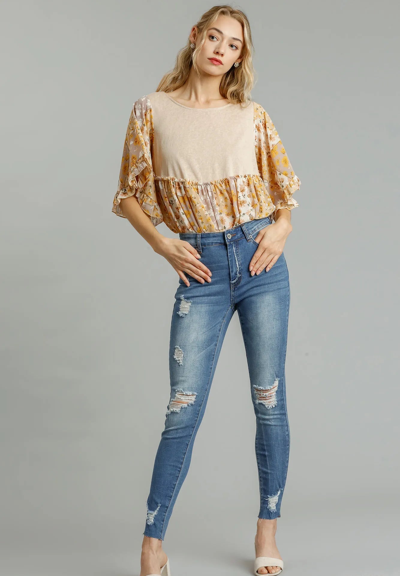 Woman wearing a patterned top and blue jeans on a gray background