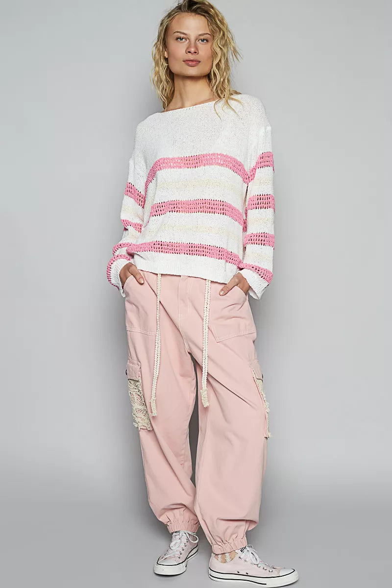 Person wearing a white sweater with pink stripes and pink pants on a gray background