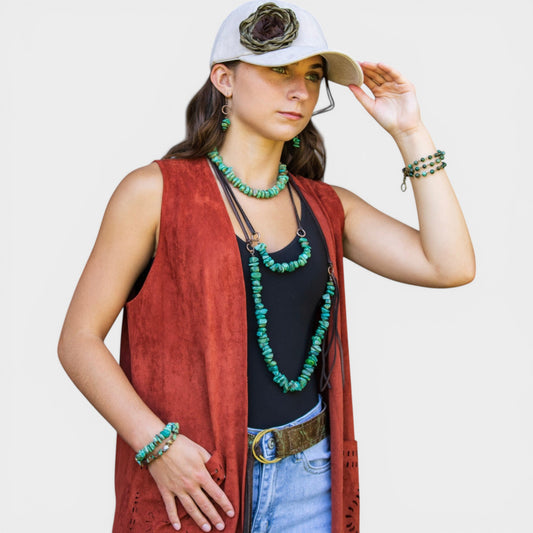 Woman wearing a red vest, black top, blue jeans, and a white cap with a flower on a plain background