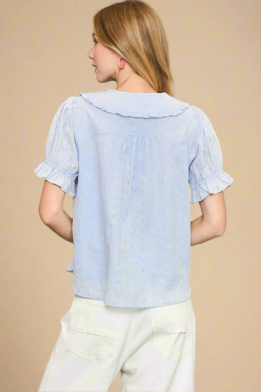 Woman wearing a light blue blouse with ruffled sleeves on a beige background