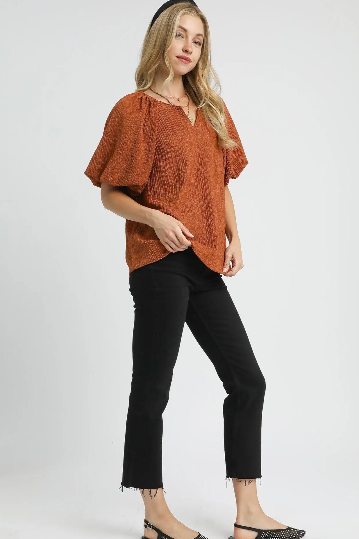 Woman wearing a rust-colored top and black pants on a white background