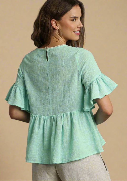 Woman wearing a light green blouse with ruffled sleeves on a beige background