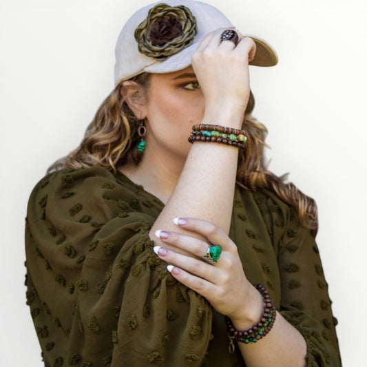 Woman wearing a green dress, white hat with a flower, and jewelry against a plain background