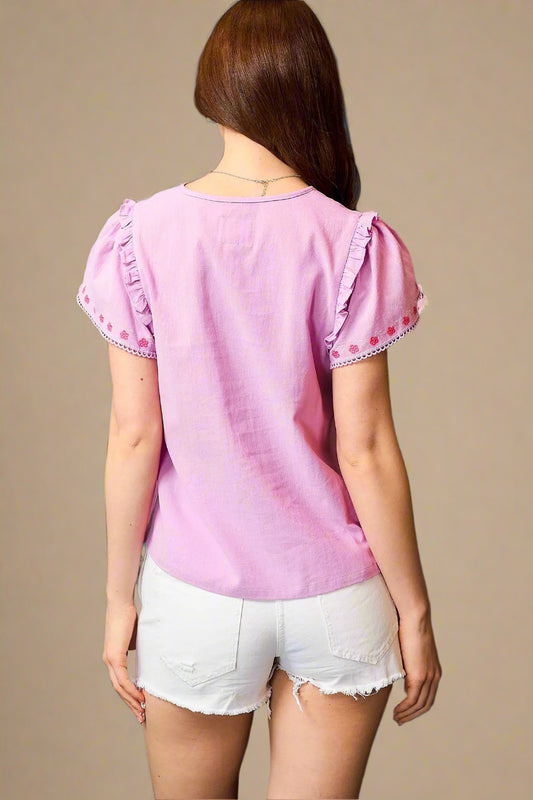 Woman wearing a pink blouse with ruffled sleeves against a beige background