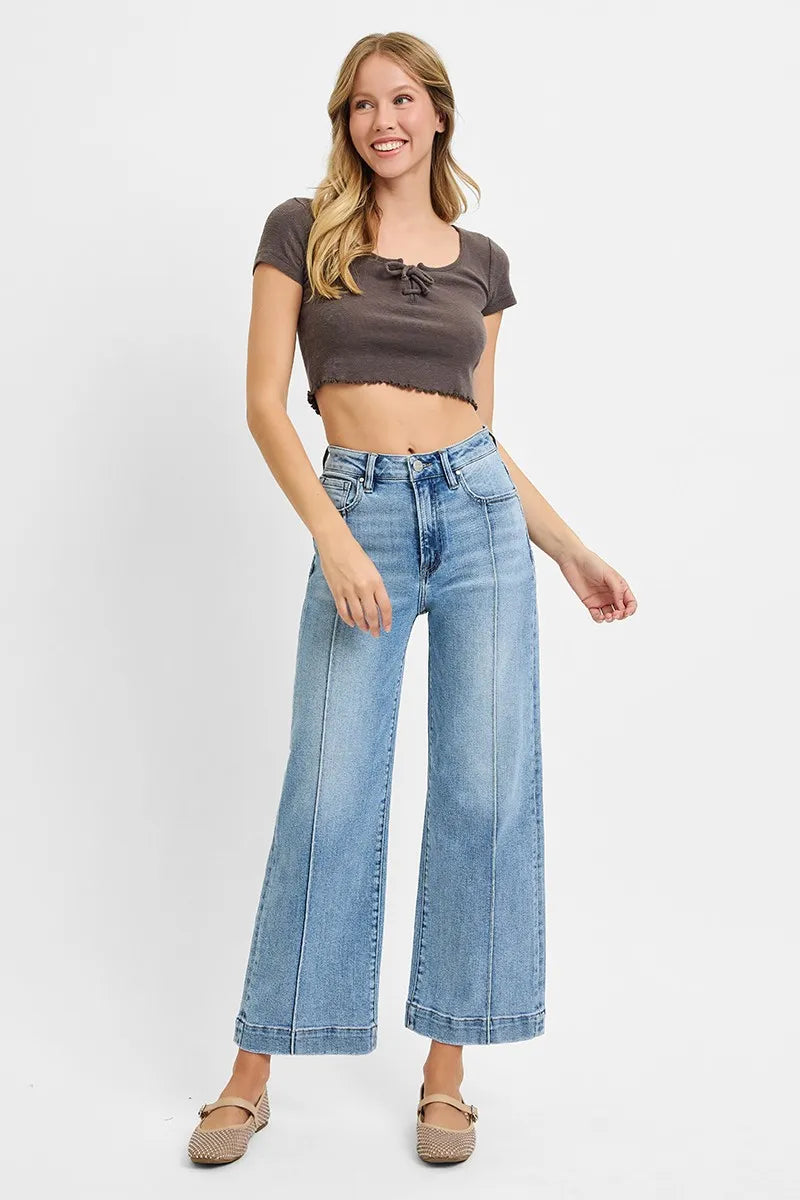 Woman wearing a brown crop top and light blue jeans on a white background