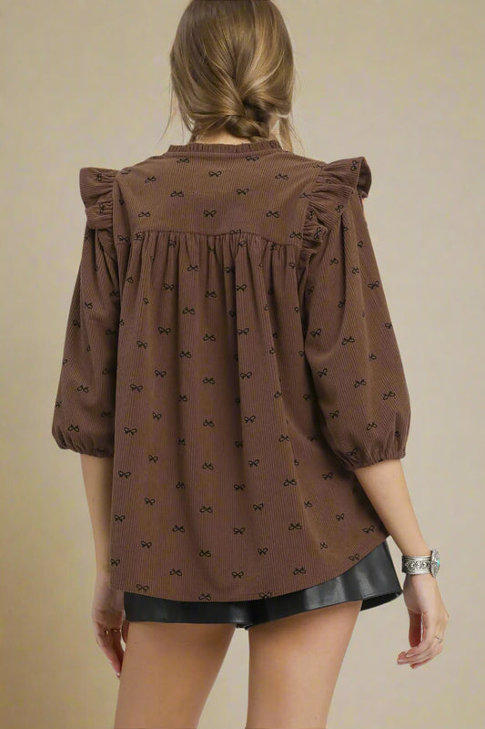 Brown blouse with black pattern worn by a person on a beige background