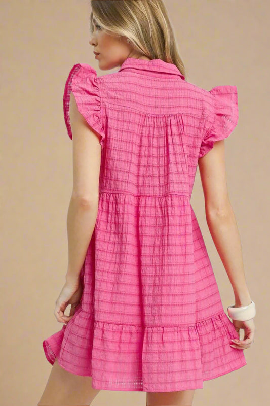 Woman wearing a pink checkered dress with ruffled sleeves on a beige background