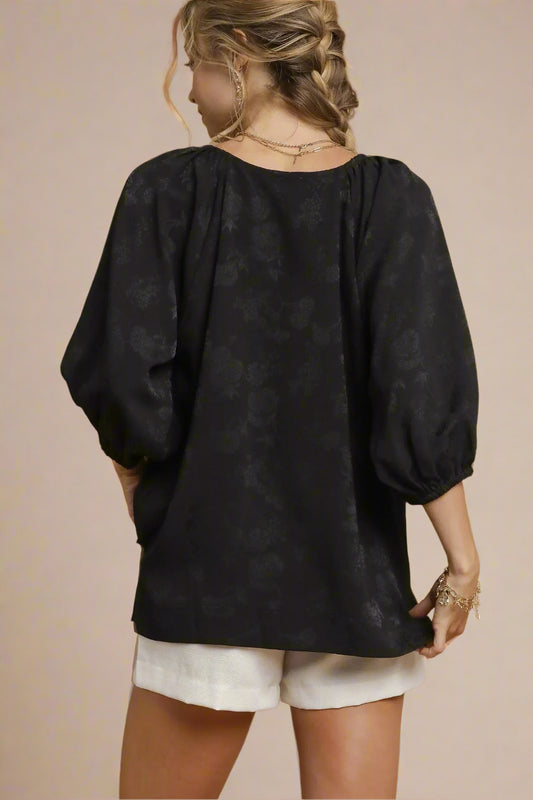 Woman wearing a black blouse with puff sleeves on a beige background