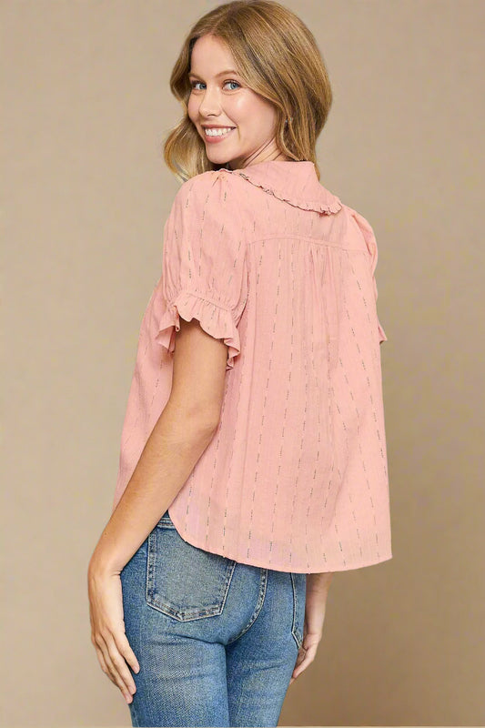 Woman wearing a pink blouse with ruffled sleeves and blue jeans against a gray background
