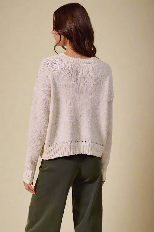 Person wearing a light gray sweater and green pants against a beige background