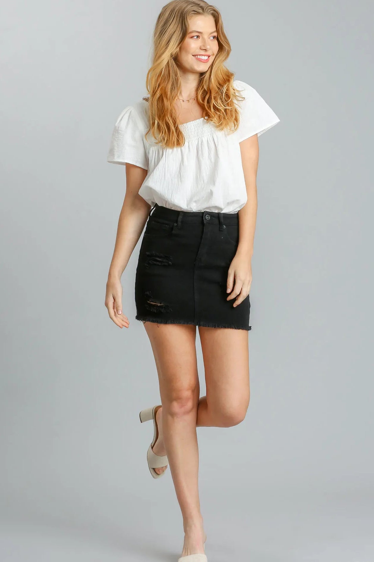 Woman wearing a white top and black skirt on a gray background