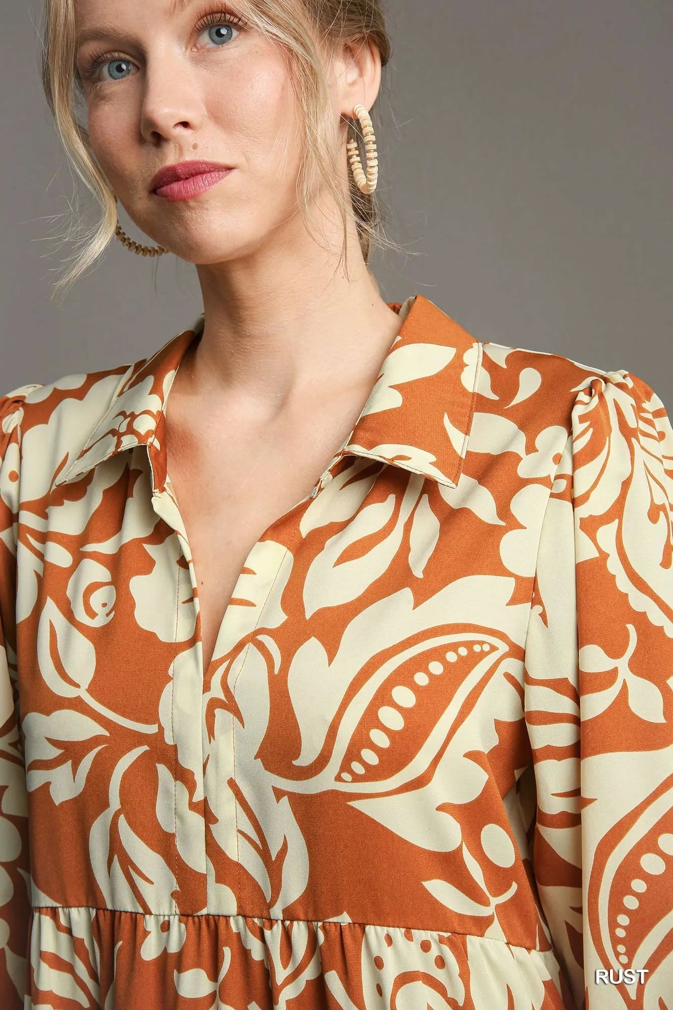Woman wearing a rust-colored dress with white floral patterns against a neutral background