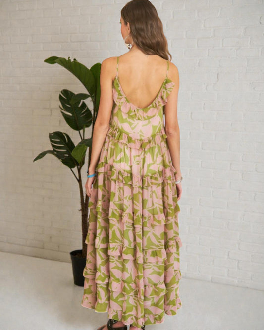 Woman wearing a floral dress standing in front of a white brick wall with a plant.