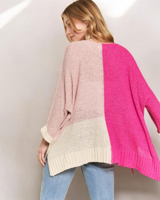 Woman wearing a color-blocked sweater with pink, beige, and white sections on a plain background.