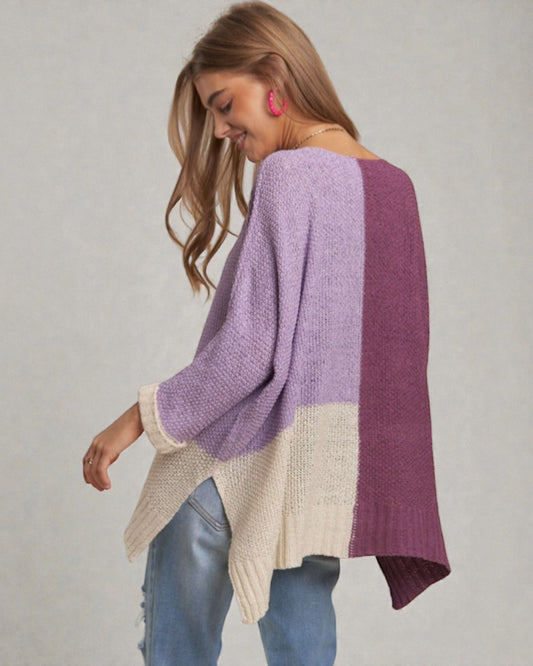 Woman wearing a color-blocked sweater with purple, beige, and blue sections on a plain background.